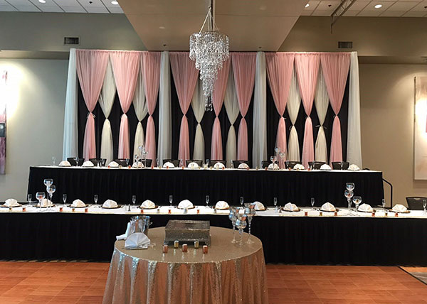 Wedding decorations with a long table and pink and white drapes.